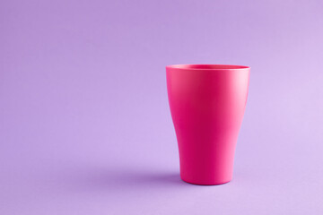 Pink plastic cup at purple background with copy space.
