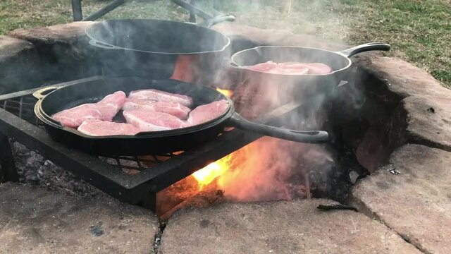 Cooking pork chops in Dutch oven cast iron skillets over an open campfire