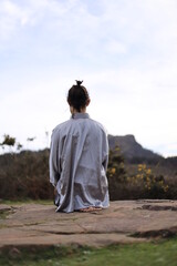 Young man in Tai Chi suit meditating on the mountain