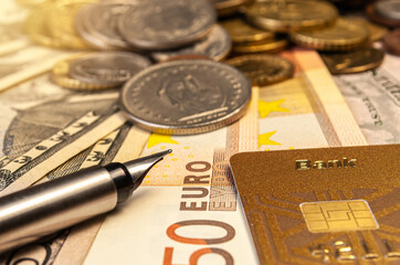 credit card and ink pen lying on a background of banknotes and coins of different currencies