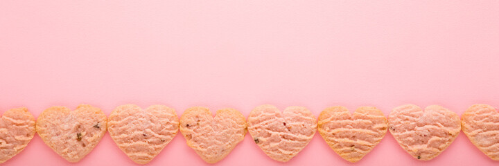 Row of heart shapes. Dry cookies on light pink table background. Pastel color. Sweet snack. Wide banner. Empty place for cute, sentimental text, romantic quote or inspirational sayings. Top down view.