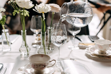 Woman pouring water from a transparent jug into a glass at a cafe.