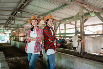 Fototapeta na wymiar a smiling boy and girl wearing a hat stand back to back in a crossed hands pose in a cow farm stable