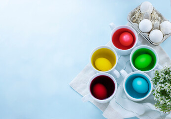 Close up of easter eggs dye process and eggs in carton against light blue background. Image with copy space