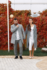 Fototapeta premium Stylish couple in gray coats walking in the autumn park. Happy sensual wedding couple. Romantic moments of newlyweds.