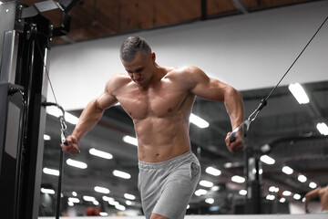 Naklejka premium Muscular athletic bodybuilder standing training chest and shoulders muscles on fitness equipment