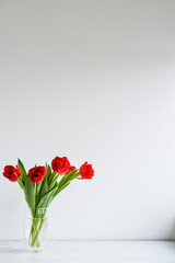 Fototapeta premium Tulip bouquet standing on the transparent glass vase on the white wooden background - Simplicity and nature