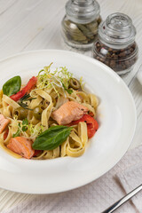 Pasta with herbs and salmon on a white wooden table
