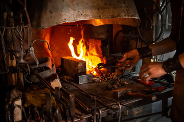 blacksmith holds billet over hot coals in clay oven. blacksmith heating iron metal sword manufacturing marching forge, Hands of blacksmith holding steel in fire of a red-hot forge