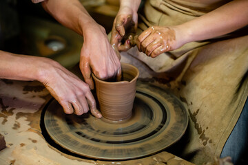 Fototapeta na wymiar Pottery classes, student making clay pot on wheel. Close-up of dirty hands, sculpting clay crockery pottery training