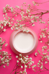 Cream for face in flowers . Face cream on a pink background. Skin care. The beauty industry. Copy space. White flowers. Article about the right choice of cream. Selection of the cream. Spa treatments.