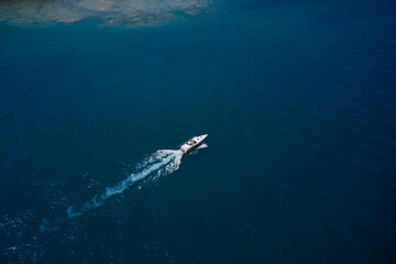 Large boat traffic along the coast. Top view of a white yacht sailing in the blue sea. Drone view of a boat sailing across the blue clear waters. Aerial view luxury motor boat.