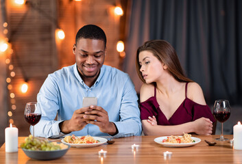 Fototapeta na wymiar Jealous young woman peeking into boyfriend's smartphone, reading his messages during dinner