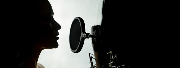 Silhouette of a woman with studio microphone. Head and shoulders side photo. Singing concept. White...