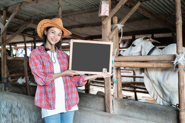 female cow farm owner holding a blackboard with a cow barn background