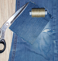 Old jeans with a hole ready to upcycling and thread. Concept of things reuse and natural resources preserving.