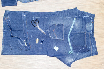 Making new kid's clothes from old ragged jeans: ripped trouser-leg, threads, scissors and chalk. Concept of things reuse and natural resources preserving.