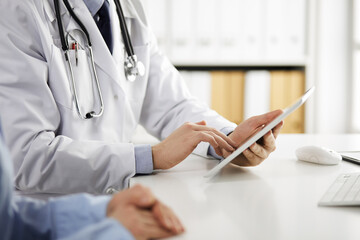 Unknown male doctor and patient woman discussing current health examination while sitting in clinic...