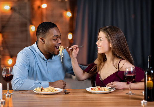 Loving Interracial Couple Feeding Each Other With Spaghetti During Dinner In Restaurant