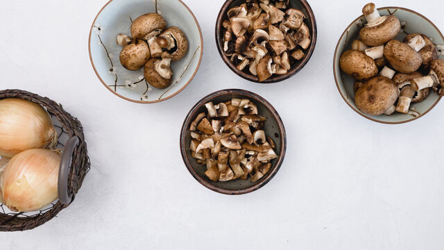 Fresh Raw Brown Mushrooms In A Bowl And Yellow Onion In Basket, Close Up View From Above With Copy Space.