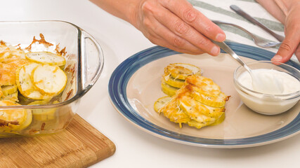 Baked zucchini on a plate close up. Zucchini slices with seasoning salt, black pepper and cheese, served with sour cream.