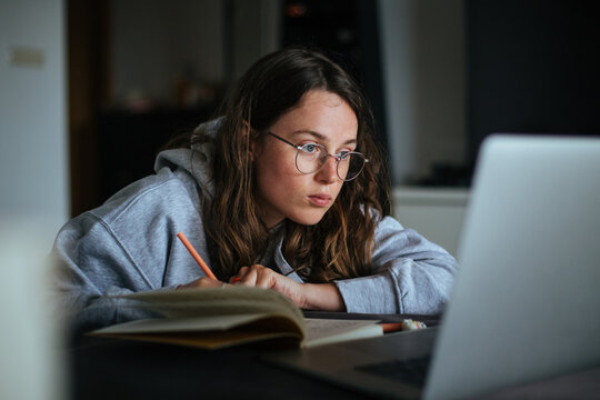Young millennial woman at home look at laptop and make notes in notebook. Learn new skill from online classes or masterclass. New generation use technology for education and freelance