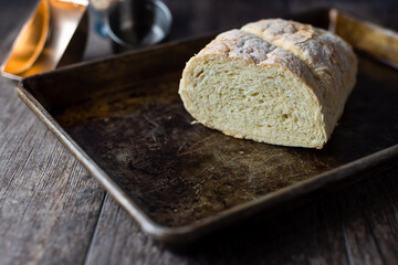 Fresh bread on a baking sheet sitting upon a wooden table top