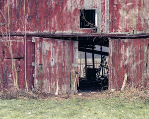 An old red barn, with peeling red paint has its doors open revealing items inside © Kimberly Boyles