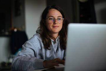 Millennial young woman sit at home and work on laptop.Home office concept, screen lit face from laptop, look at website and learn new skills from internet.Technology and information overload, big data