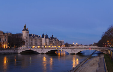 View of Paris by night with a bridge over the Seine river and the Conciergerie building.
