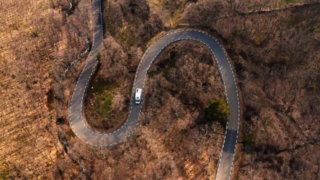Cinematic drone shot of white camper RV van on scenic mountain road. Beautiful inspiring aerial shot of autumn fall forest road winding in national park. Vanlife outdoor lifestyle concept