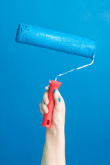 Hand with paint roller on light blue painted surface