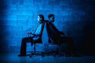 Bad relationship concept. Man and woman in disagreement. Young couple after a quarrel sitting on chairs back to back. Businessmen and partners did not share anything. Blue filter