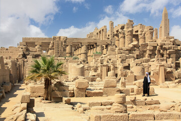 An elderly Egyptian stands in the middle of the historical temple complex of Karnak. He wears a...