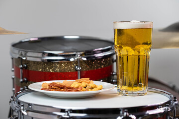 Glass of light beer with salty snacks on professional drum set closeup. Drumsticks, drums and cymbals, at live music rock concert, in the club stage, bar, or in recording studio