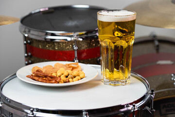Glass of light beer with salty snacks on professional drum set closeup. Drumsticks, drums and cymbals, at live music rock concert, in the club stage, bar, or in recording studio