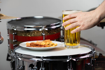 Glass of light beer with salty snacks on professional drum set closeup. Drumsticks, drums and cymbals, at live music rock concert, in the club stage, bar, or in recording studio