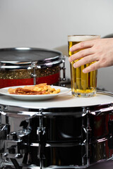 Glass of light beer with salty snacks on professional drum set closeup. Drumsticks, drums and cymbals, at live music rock concert, in the club stage, bar, or in recording studio