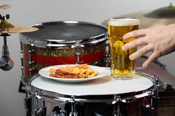 Glass of light beer with salty snacks on professional drum set closeup. Drumsticks, drums and cymbals, at live music rock concert, in the club stage, bar, or in recording studio