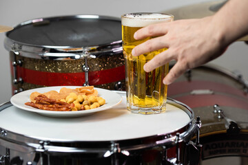 Glass of light beer with salty snacks on professional drum set closeup. Drumsticks, drums and cymbals, at live music rock concert, in the club stage, bar, or in recording studio