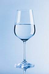 Wine glass. Blue background. Half filled with clear lilquid.