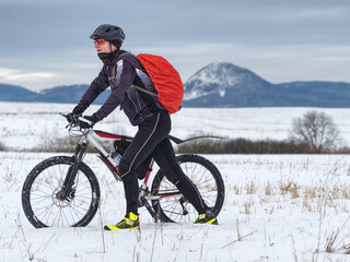 Adult athlete pushes MTB through the snow across a frozen meadow. Biker can't ride in free terrain