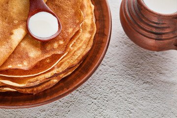 Pancakes. Thin pancakes for breakfast top view. Russian traditional pancakes. East Slavic traditional holiday Maslenitsa. A spoonful of sour cream and a bowl of milk.