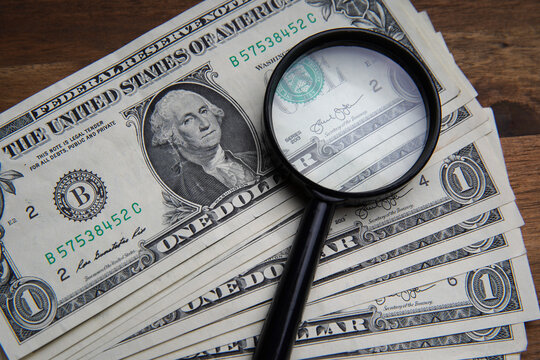 A portrait through the magnifying glass of a dollar is a portrait of the late American President George Washington. Bank image and commercial photo on brown wooden table background.