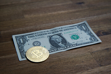 Pile of american dollars cash on brown wooden table. Next to it is a gold bitcoin digital cryptocurrency coin. Bank image and photo background.