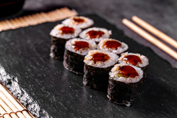 Maki Sushi Rolls with eel on black stone on dark background. Sushi menu. Japanese food. Closeup of delicious japanese food with sushi roll. Horizontal photo