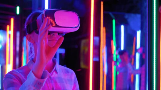 VR, futuristic, retrowave, immersive, entertainment concept. Woman using virtual reality headset and looking around at interactive technology exhibition with colorful illumination