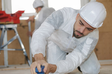 young handyman sanding wooden floor in workshop