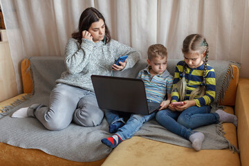 Mother with kids sitting on coach and cutting loose on social media platforms, audio, message and video chatting on laptop and smartphone, social media in everyday life, new audio chat, focus on kid