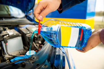 The car driver's hands refilling the blue non-freezing windshield washer liquid in the tank of the car on a winter sunny day 
